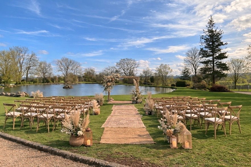 Cérémonie laïque au bord de l'étang : arche fleurie, chaises croisées et allée de tapis